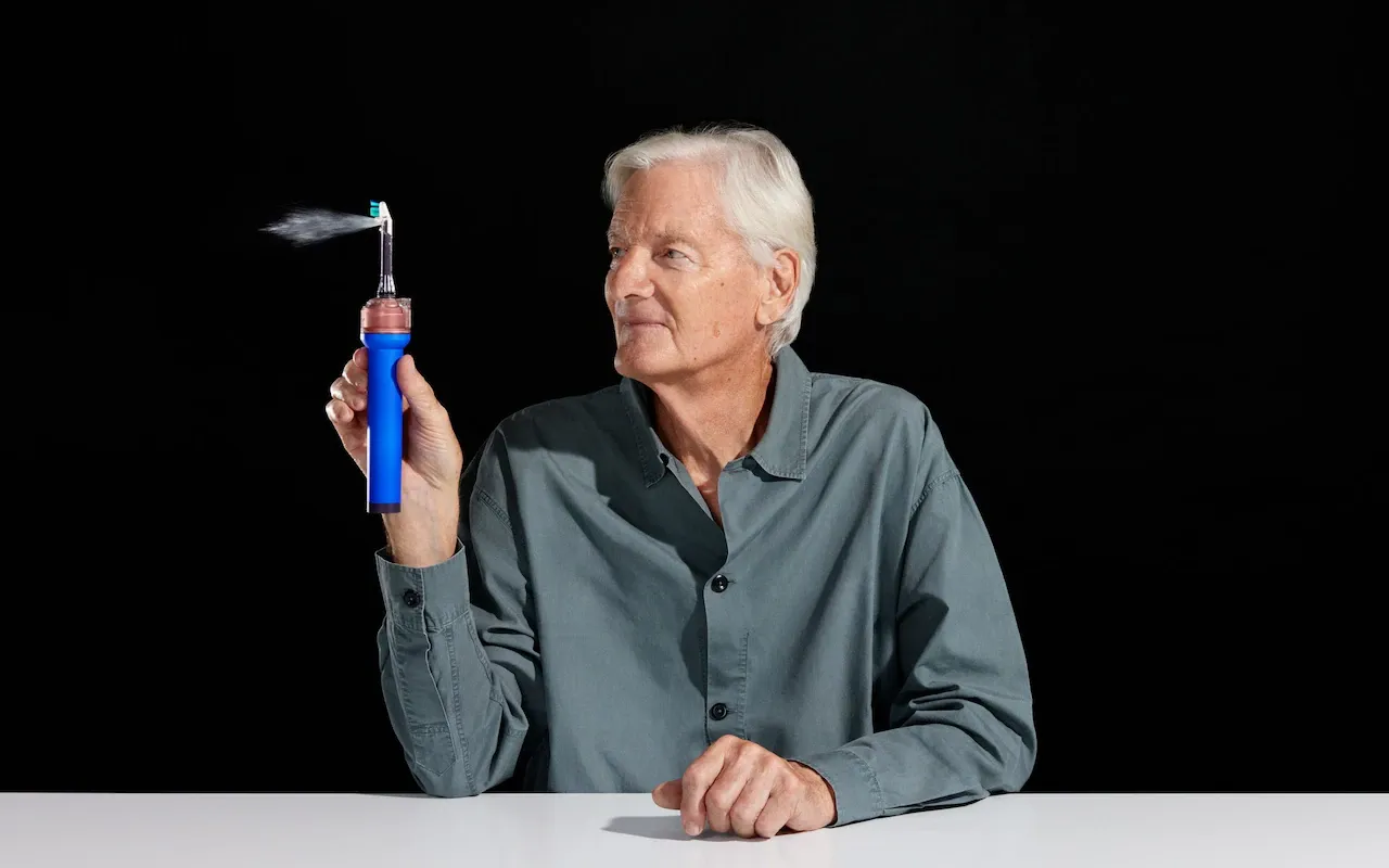 Sir James Dyson holding the CameraJet, with a fine mist firing from the brush head